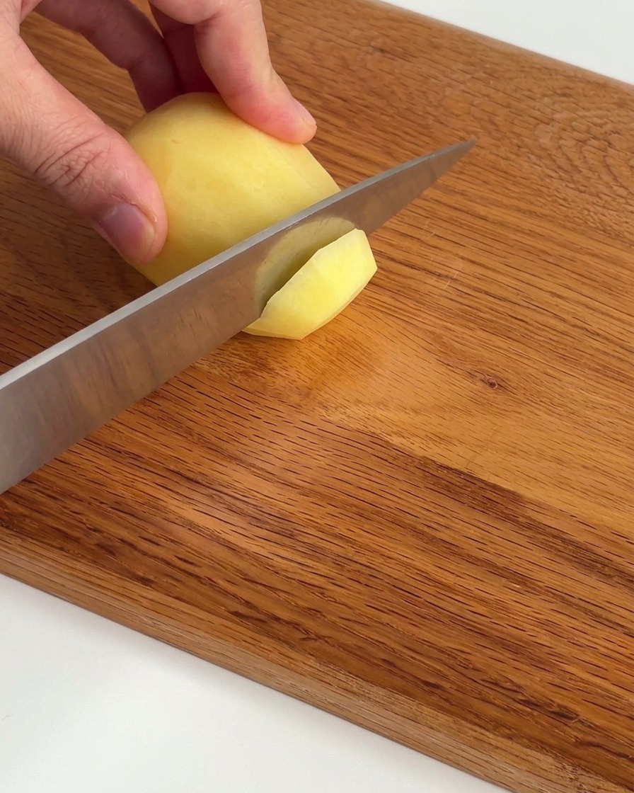 Fines tranches de pommes de terre crues soigneusement disposées sur une planche à découper en bois.