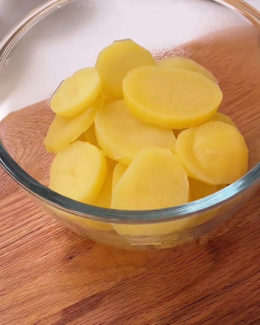 Tranches de pommes de terre cuites à la vapeur dans un bol, parsemées de poivre noir et de fécule blanche.