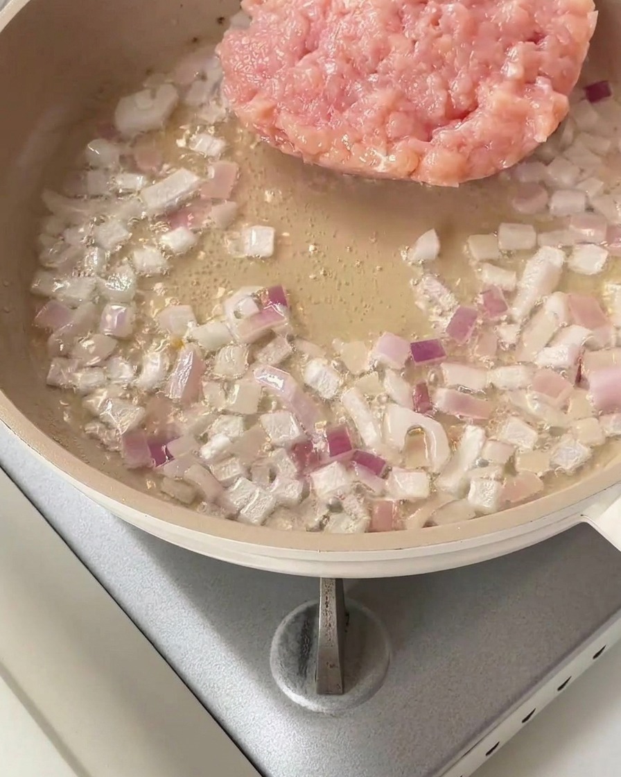 Un tas de poulet haché cru placé dans une poêle avec des oignons rouges sautés.