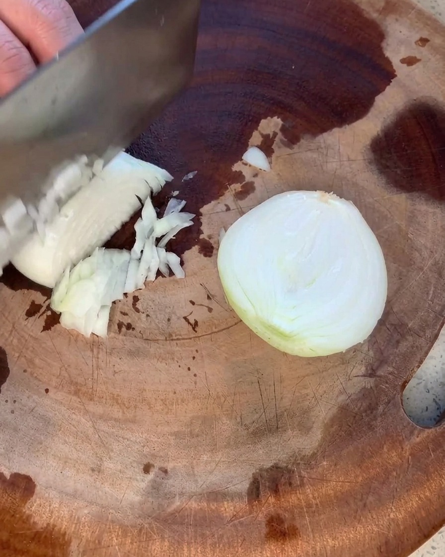 Un oignon jaune soigneusement haché en petits morceaux réguliers sur une planche à découper en bois.