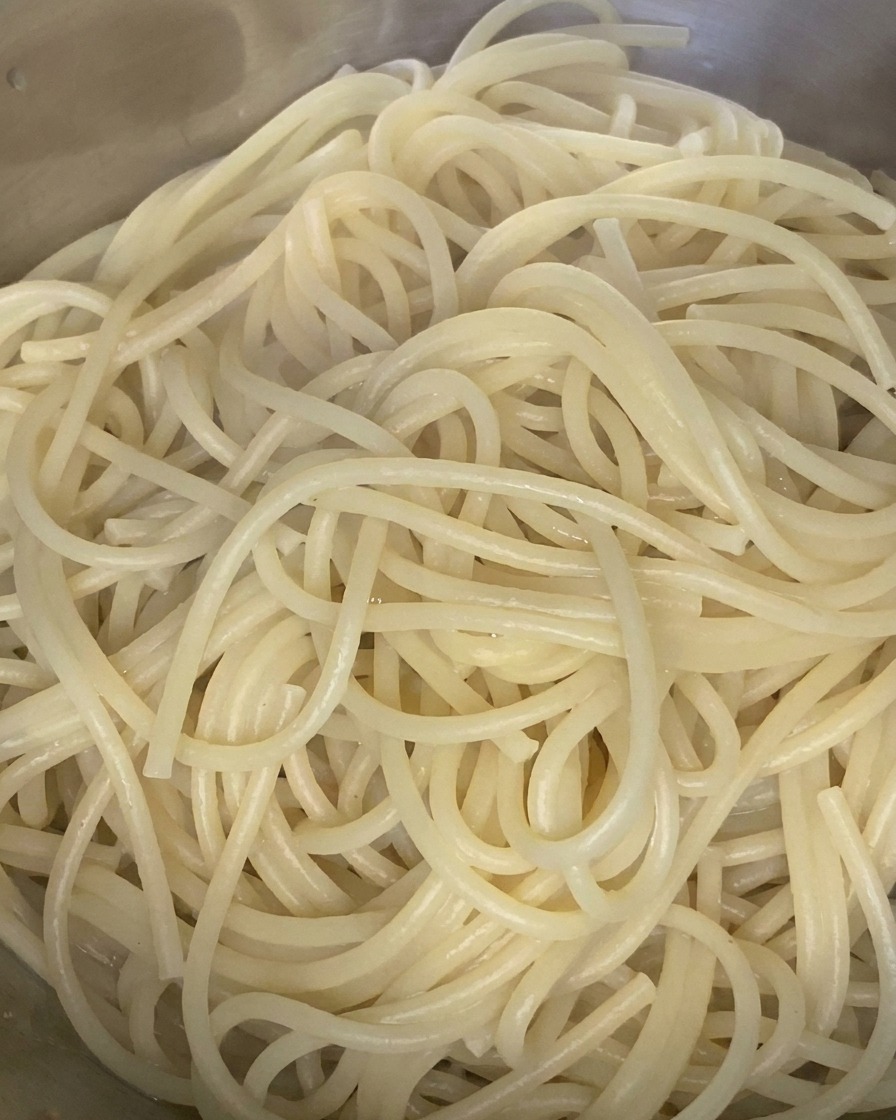Des spaghettis cuits mélangés avec un filet dhuile dolive dans un bol en acier inoxydable.