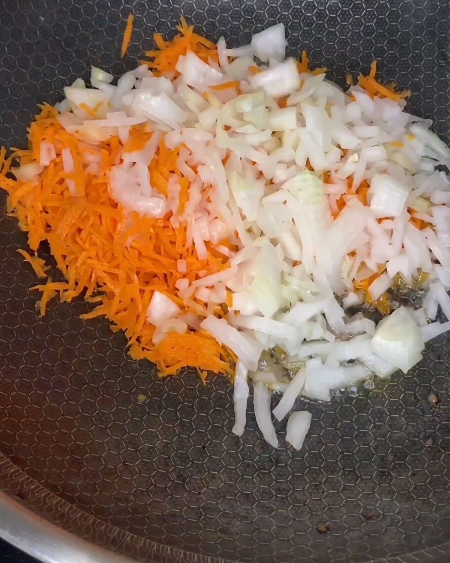 Un mélange de carottes râpées et doignons hachés qui ramollit dans une poêle à feu moyen.