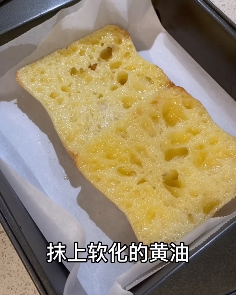Du beurre pommade étalé sur la surface du pain ciabatta sur une plaque de cuisson.