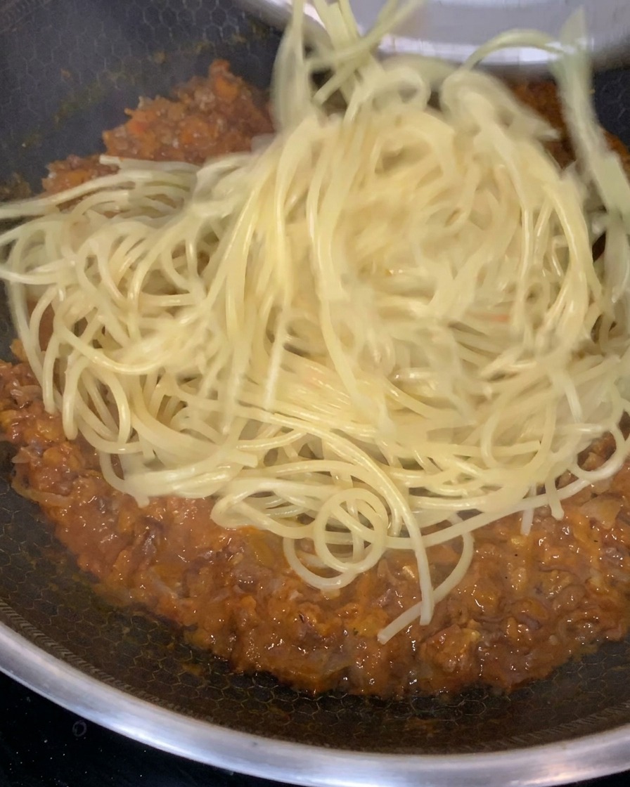 Pâtes cuites mélangées à une sauce viande riche et épaisse dans une grande poêle.