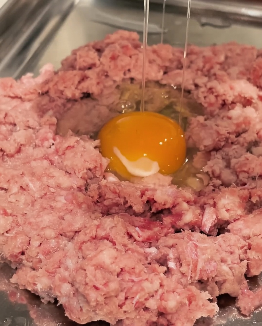 Un œuf cru cassé dans un bol de bœuf haché.