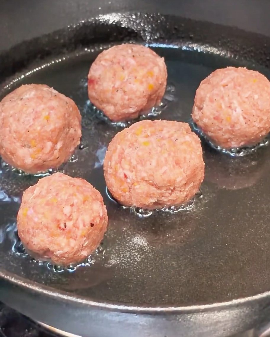 Boulettes de viande crues dorer dans une poêle huilée chaude.