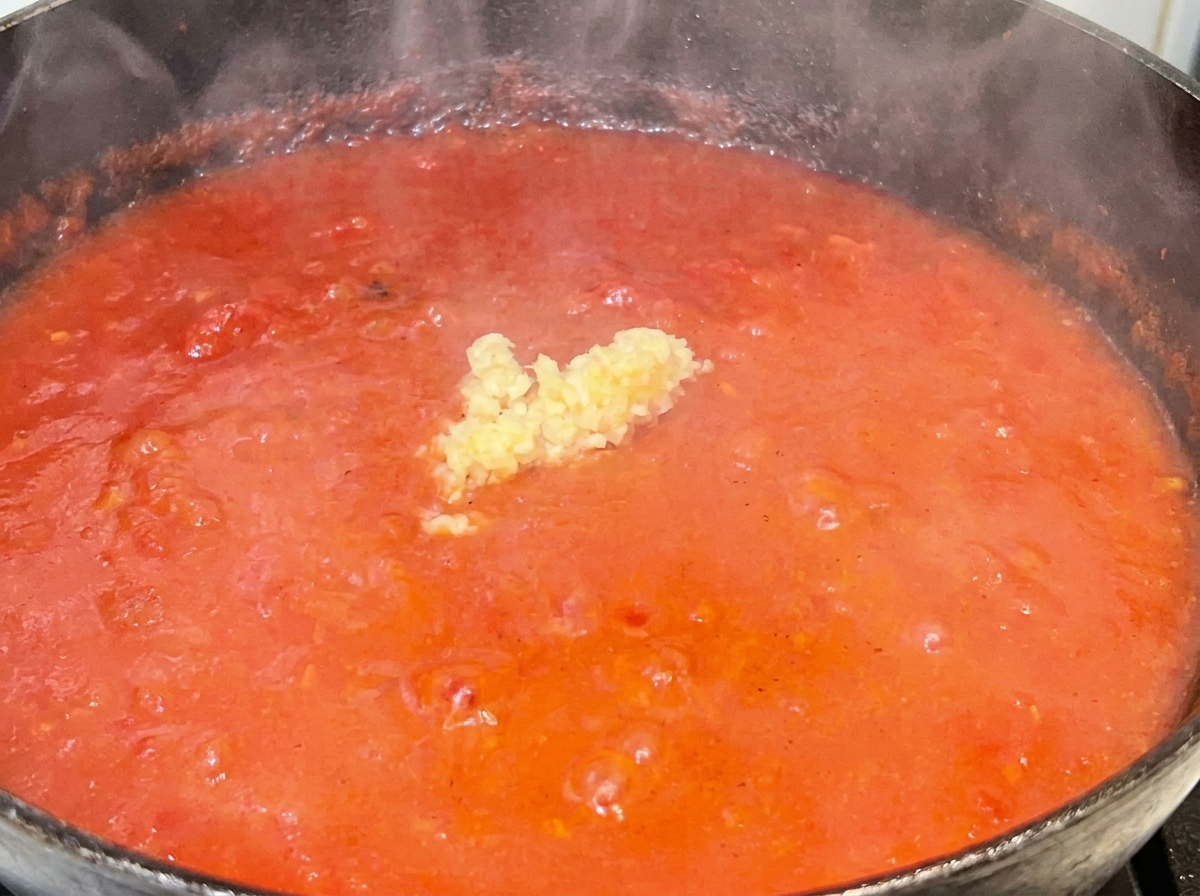 Un petit tas dail émincé au centre dune sauce tomate rouge frémissante.