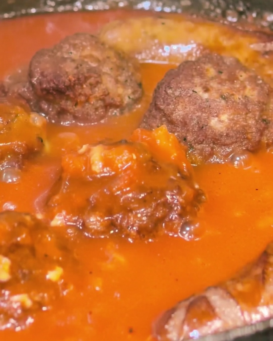 Gros plan dune poêle contenant des boulettes et des saucisses arrosées dune sauce tomate rouge épaisse.