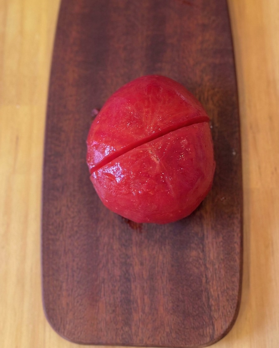 Une tomate pelée et noircie sur une planche à découper en bois après avoir été coupée en deux.