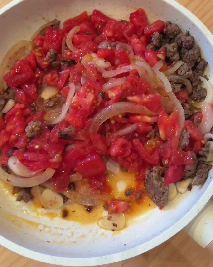 Une poêle contenant de la viande hachée dorée, des oignons, de lail et des tomates fraîchement coupées.