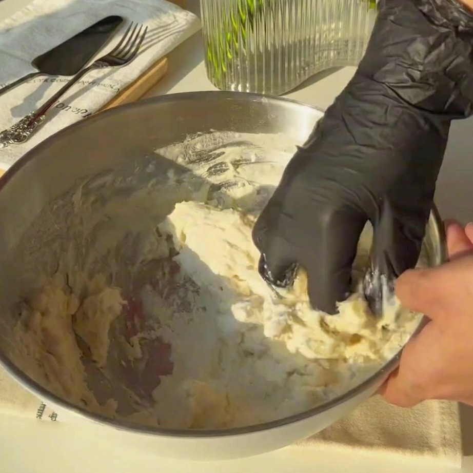Pâte grossière pétrie à la main dans un grand bol mélangeur en métal.