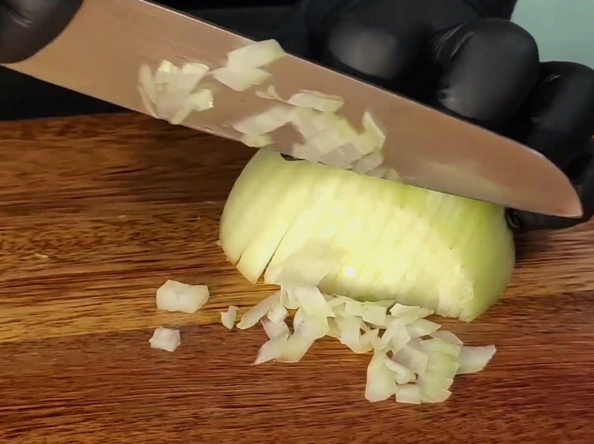 Un couteau coupant un oignon sur une planche à découper en bois.