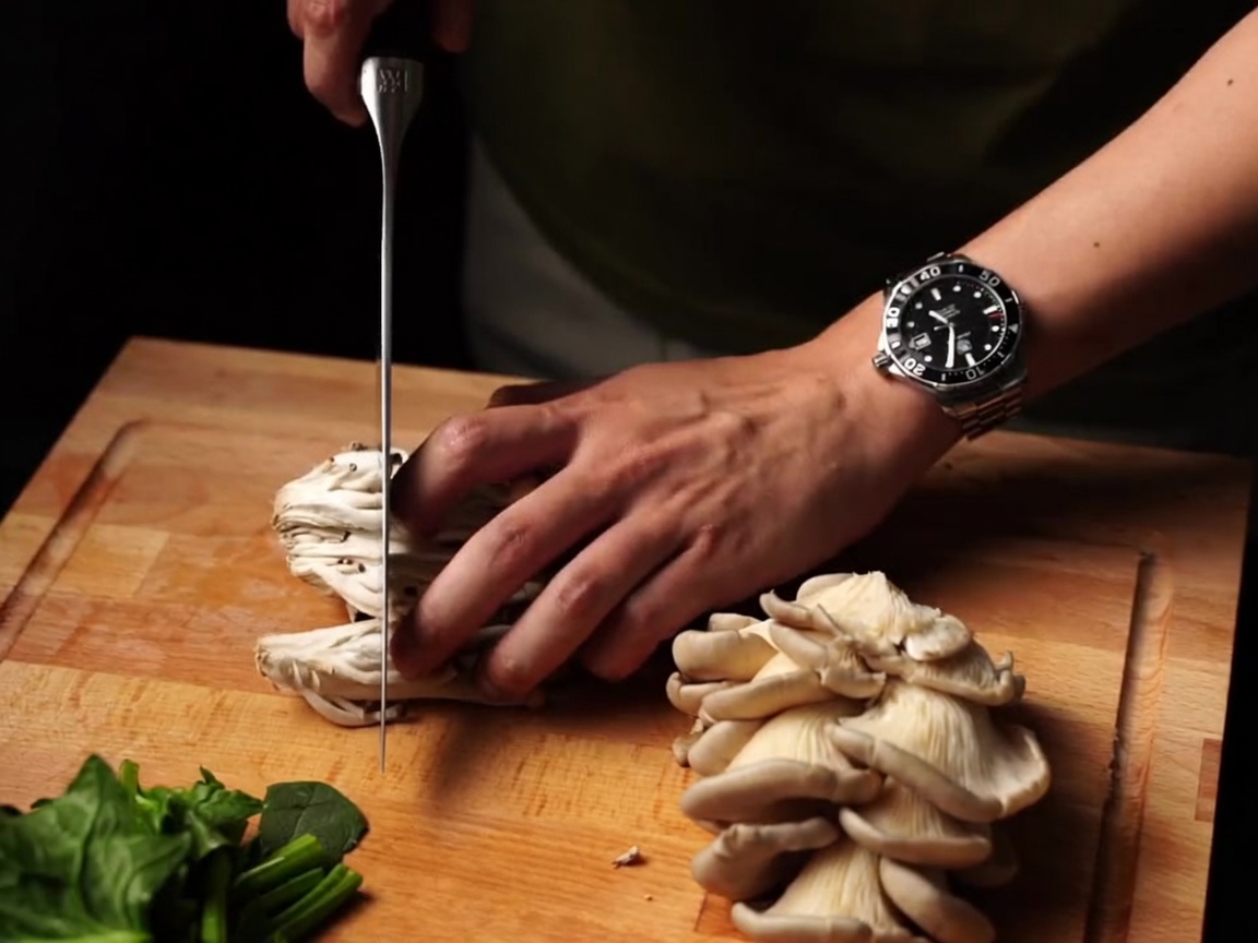 Champignons frais émincés avec un couteau sur une planche en bois.