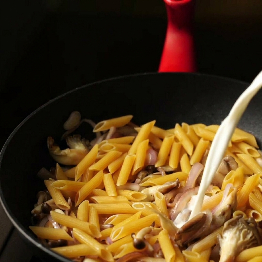 Un filet constant dun mélange deau et de lait versé dans une sauteuse sur des pennes crues et des légumes.