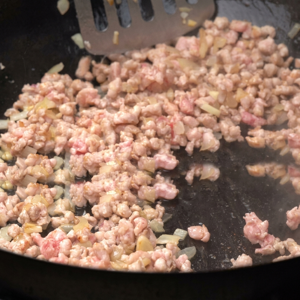 Viande hachée en train de dorer dans une poêle avec des oignons, en train dêtre remuée.