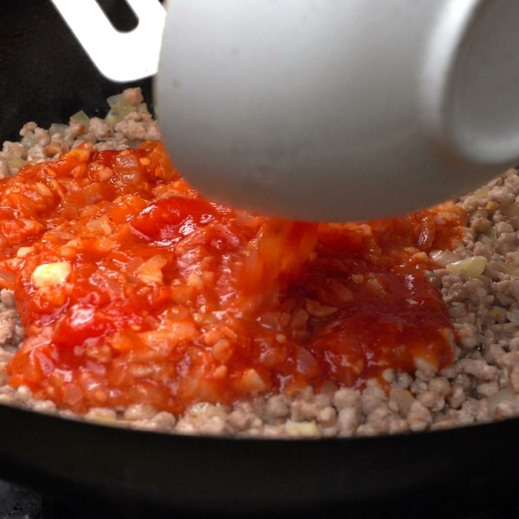Tomates concassées vibrantes versées dun bol blanc dans une poêle de viande hachée cuite.