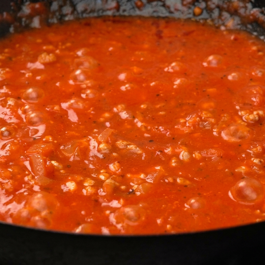 Paccheri cuits mélangés dans une sauce tomate à la viande épaisse et rouge dans une poêle.