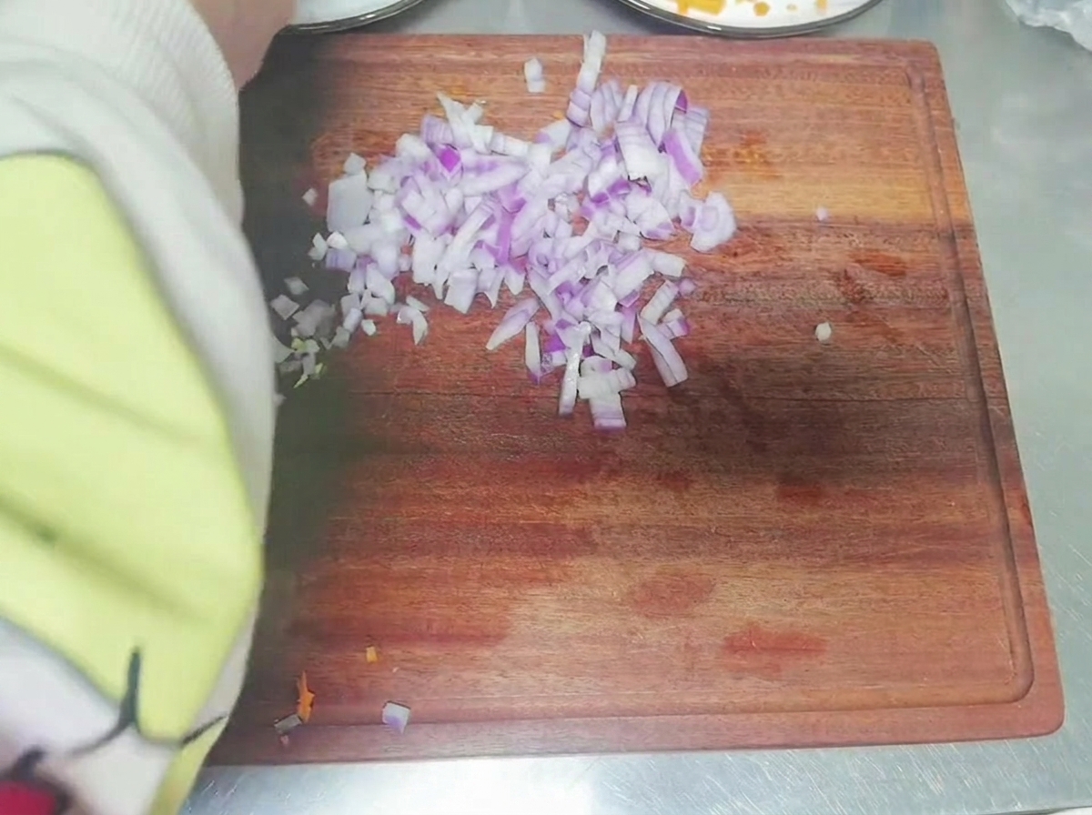Main coupant un oignon rouge en petits dés sur une planche à découper en bois.