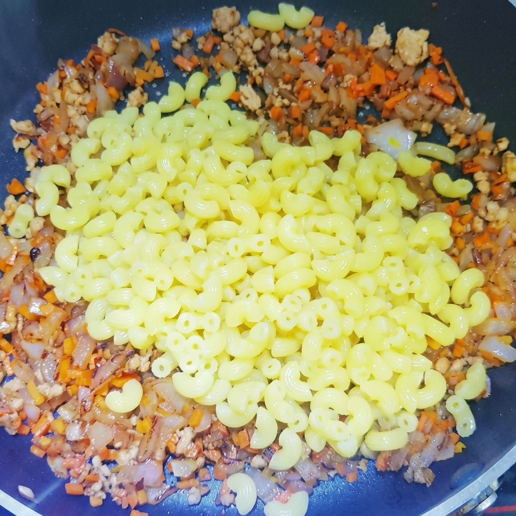 Macaronis cuits ajoutés dans la poêle avec la préparation de viande et légumes.