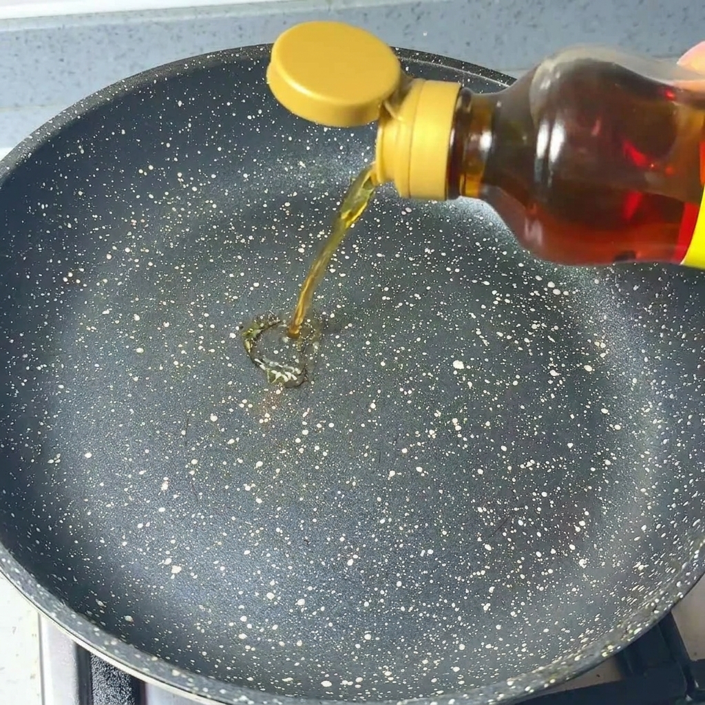 De lhuile de sésame claire versée dune bouteille dans une poêle foncée mouchetée.