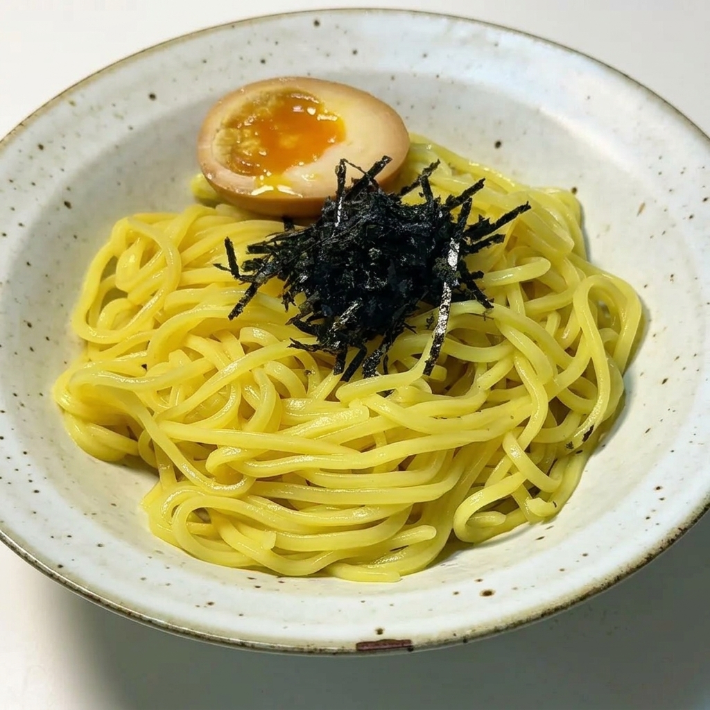 Nouilles ramen dressées garnies dun tas dalgues noires effilochées et dun œuf mollet parfaitement coupé en deux au jaune coulant.