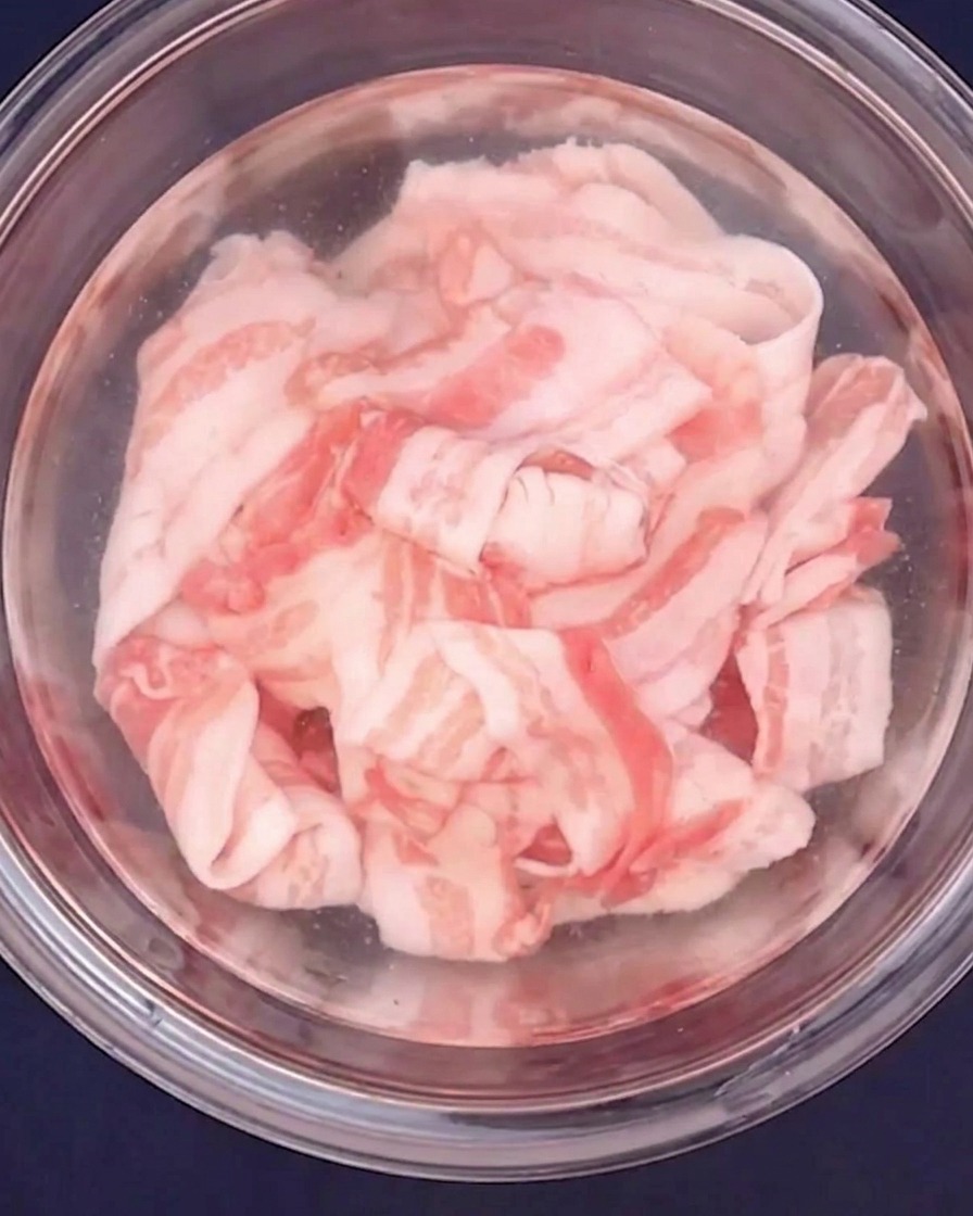 Poitrine de porc finement tranchée blanchie à leau chaude dans un bol en verre.