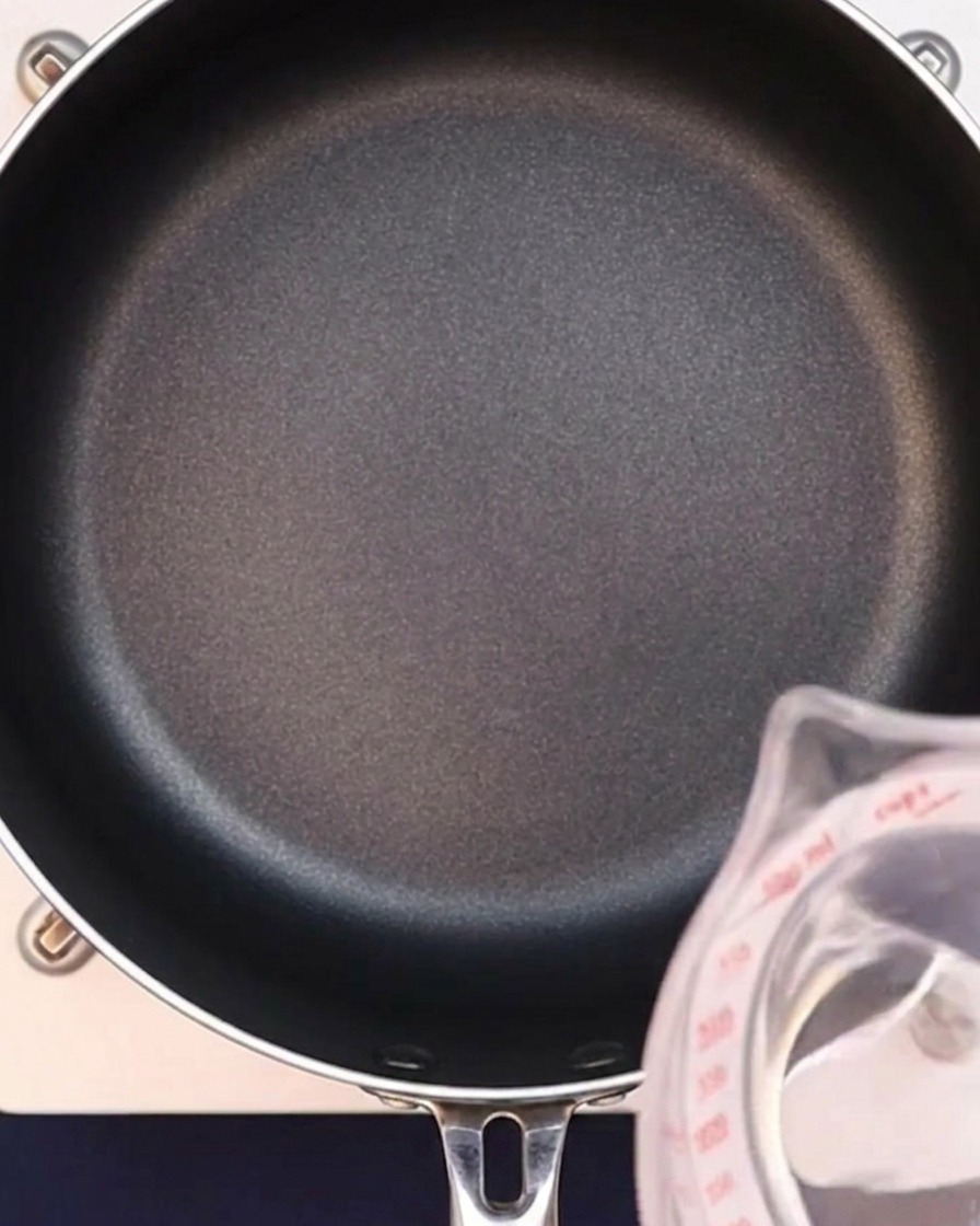 Eau versée dans une poêle noire pour démarrer le bouillon au curry.