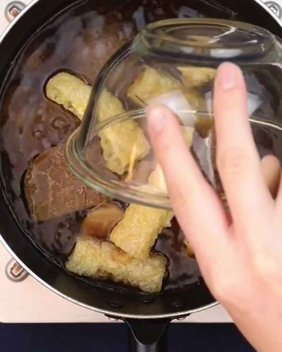 Puffs de tofu frit plongés dans une casserole de bouillon de curry japonais frémissant.