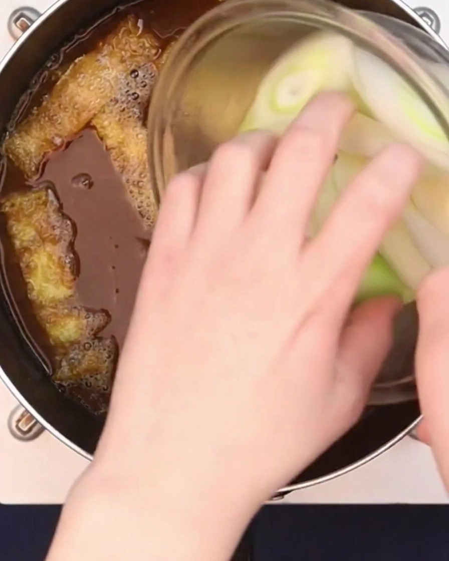 Gros oignons verts coupés en biseau ajoutés au bouillon de curry frémissant.