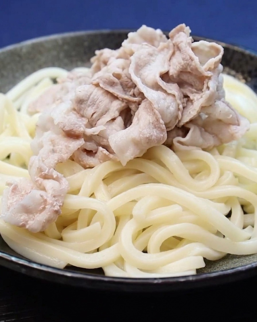 Tranches de poitrine de porc cuites déposées sur un lit de nouilles udon.