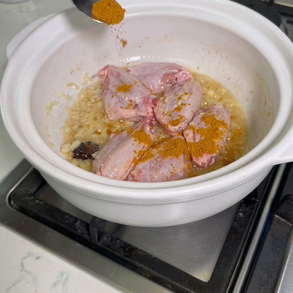 De la poudre de curry saupoudrée sur des ailes de poulet dans un faitout.