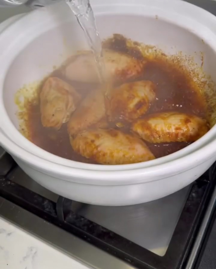 De leau claire versée dun récipient dans un faitout bouillonnant rempli dailes de poulet au curry.
