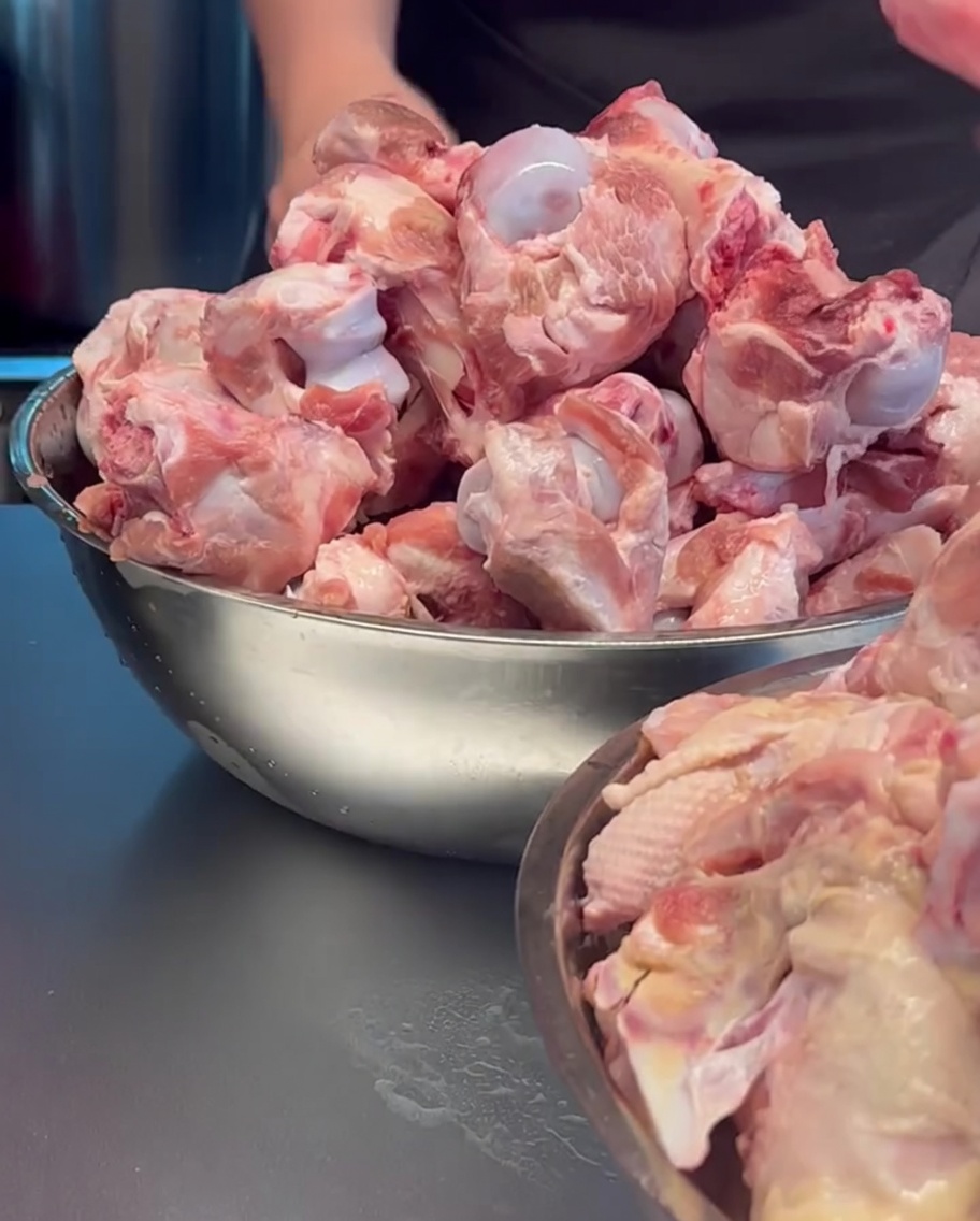 Os de porc et carcasses de poulet bruts chargés dans une grande marmite en métal.