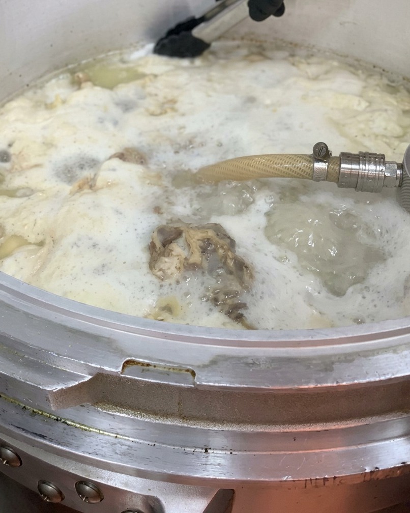 Huile de poulet versée dans la grande marmite de bouillon.