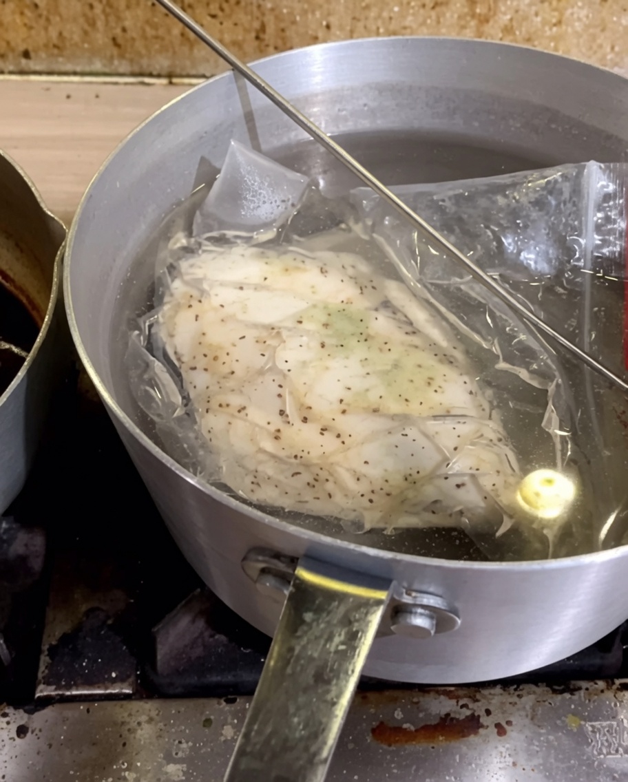 Un sac sous vide contenant le poulet assaisonné immergé dans une casserole deau chaude.