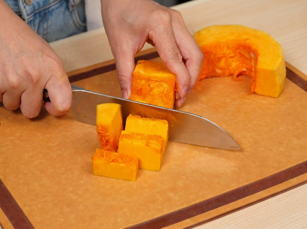 Morceaux de potiron orange frais soigneusement découpés en cubes réguliers sur une planche à découper en bois.