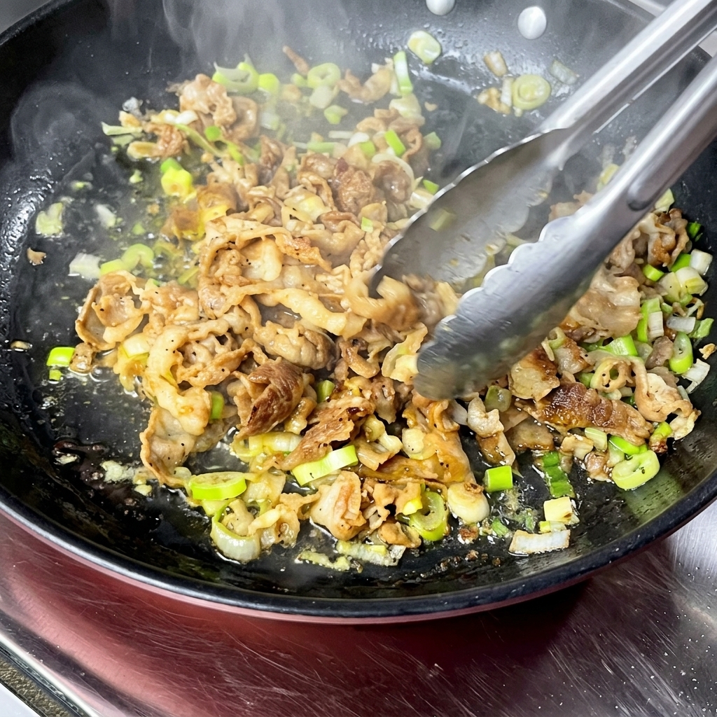 Des tranches de bœuf Angus sautées avec des oignons verts dans une poêle chaude à laide de pinces de cuisine.