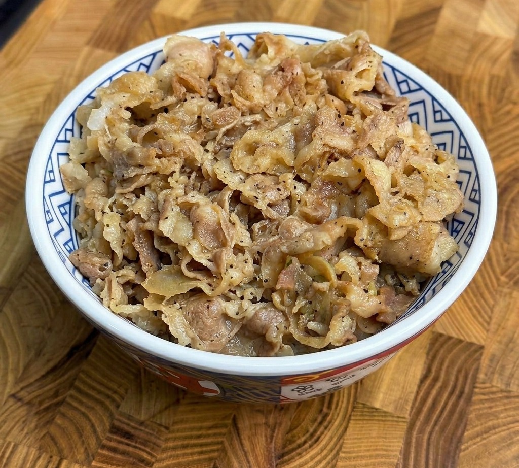 Une généreuse portion de bœuf cuit et doignons verts servie sur du riz blanc dans un bol en céramique à motifs.