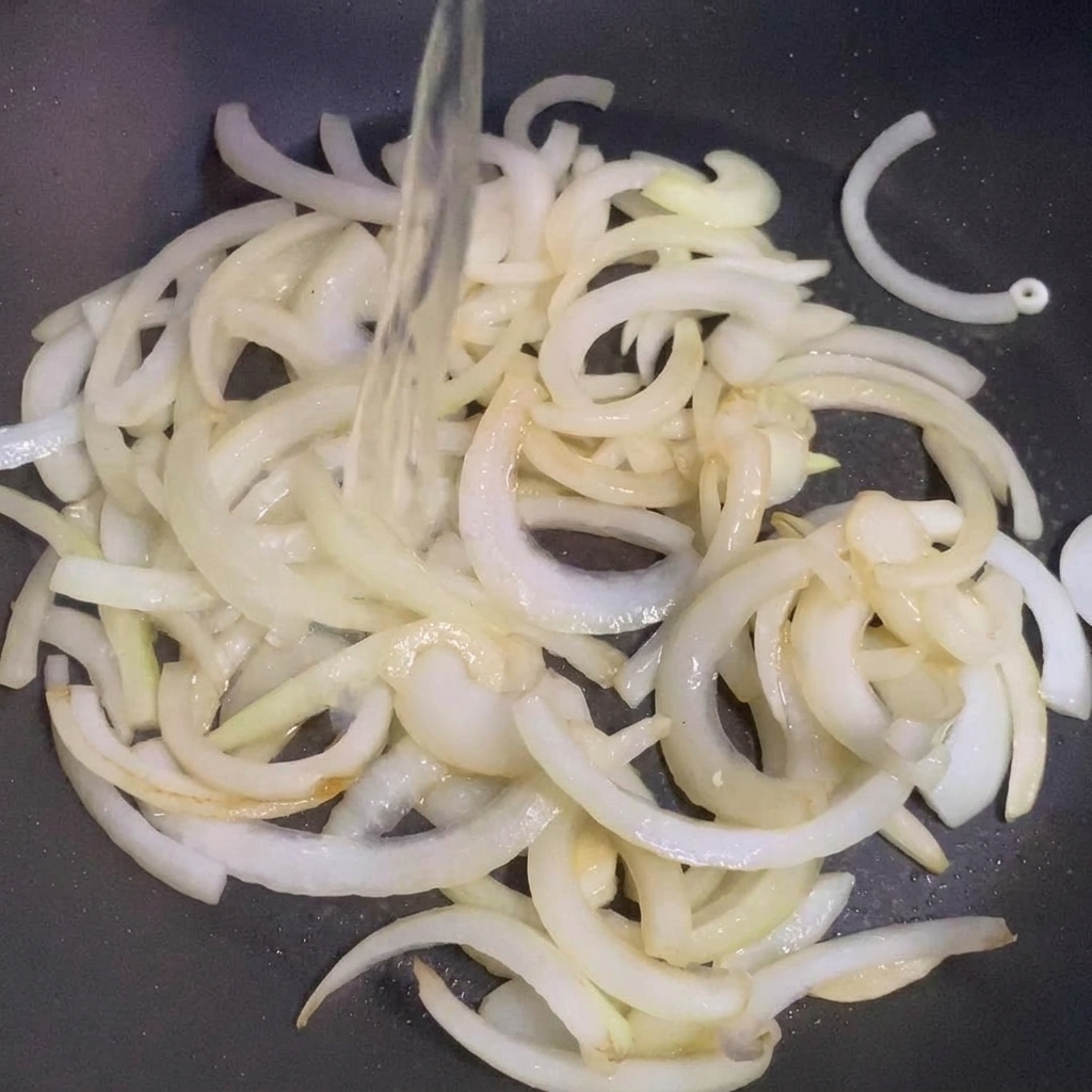 Saké versé dans une poêle contenant les oignons sautés.
