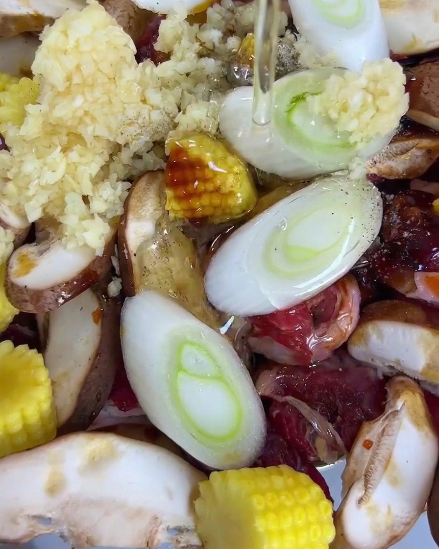 Huile de cuisson versée sur un plateau contenant du bœuf, des shiitakés, du maïs, des oignons verts et de lail.