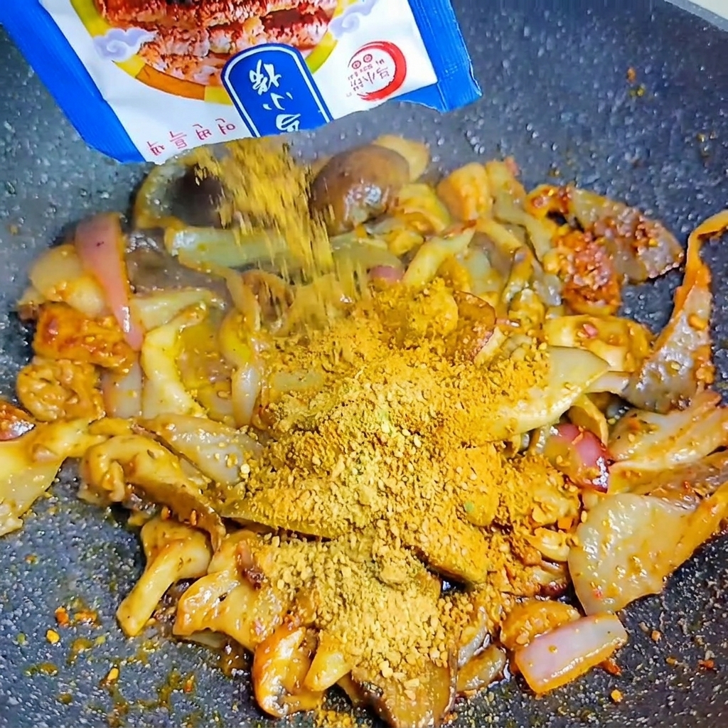 Un sachet bleu versant de la poudre dassaisonnement BBQ coréen sur les champignons et oignons.