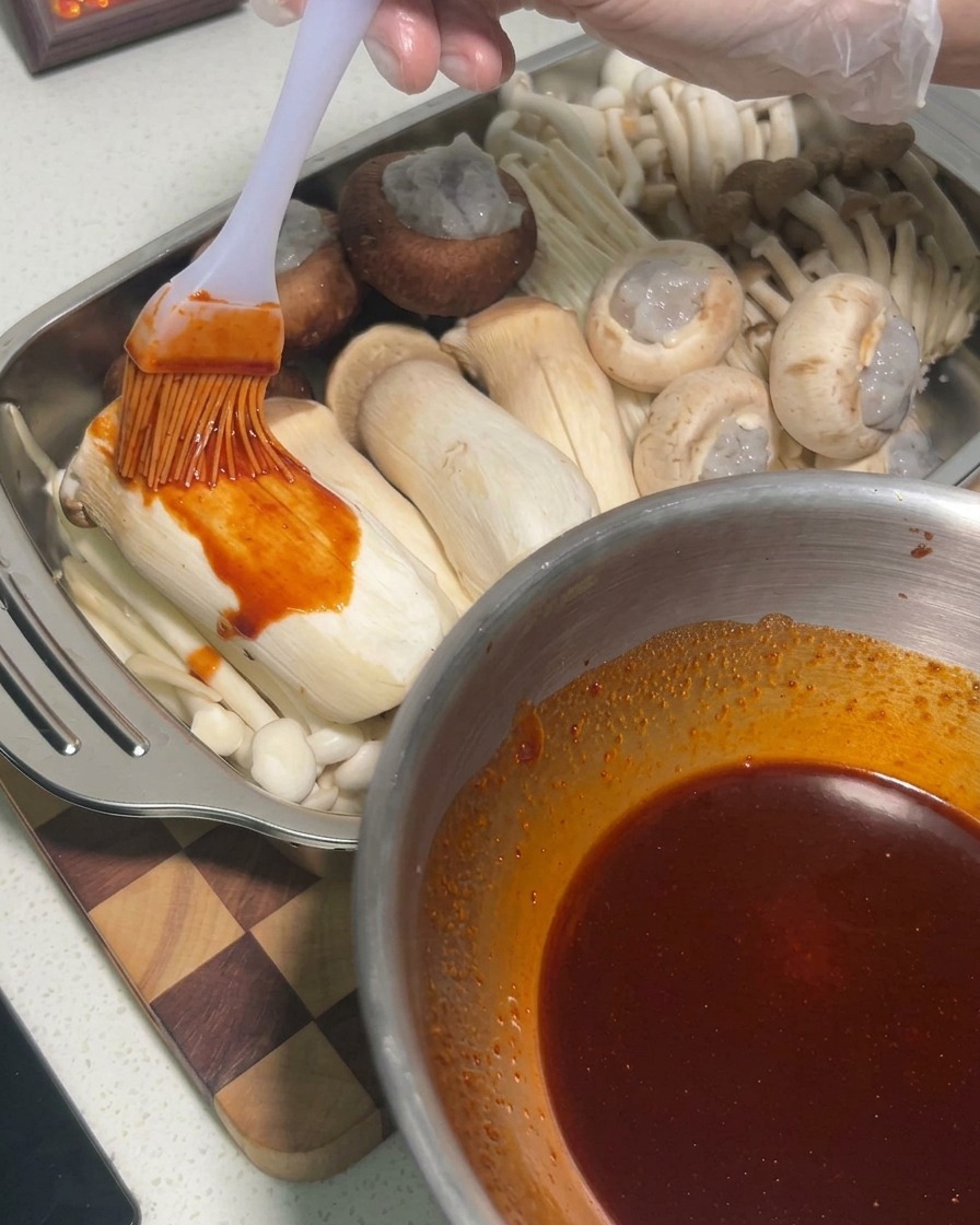 Sauce appliquée au pinceau sur des pleurotes crus à lintérieur dun plateau en métal.