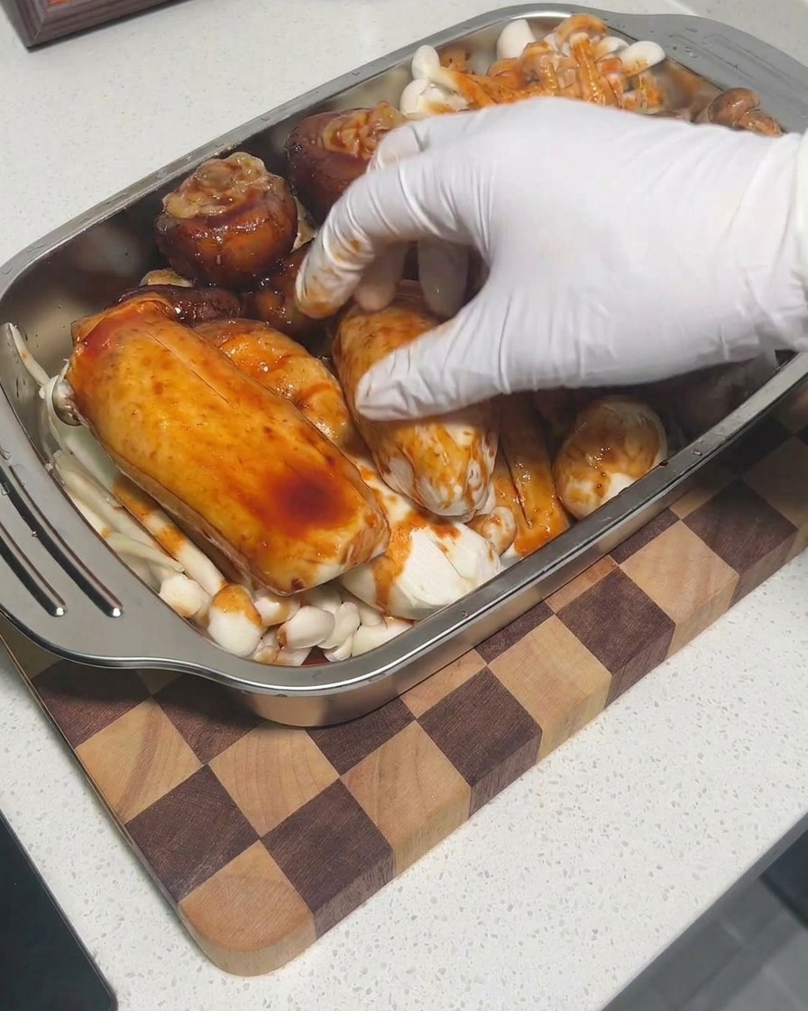 Mains gantées massant la sauce sur les champignons dans un plateau pour assurer un enrobage complet.
