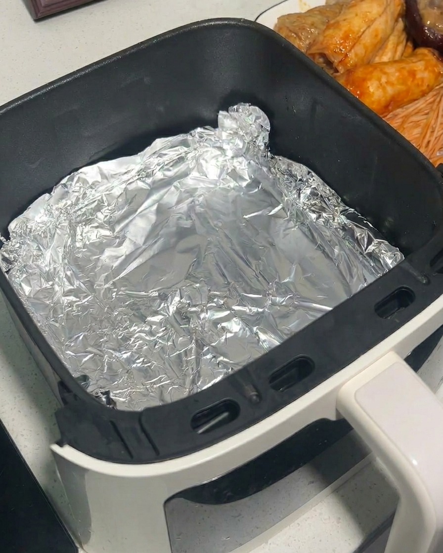 Champignons marinés placés dans un panier dair fryer tapissé de papier aluminium à laide dune pince en métal.