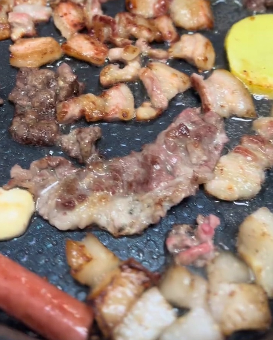 Poitrine de porc, chapeaux de champignons et tranches de pommes de terre grésillant sur un grill électrique avec une belle coloration dorée.