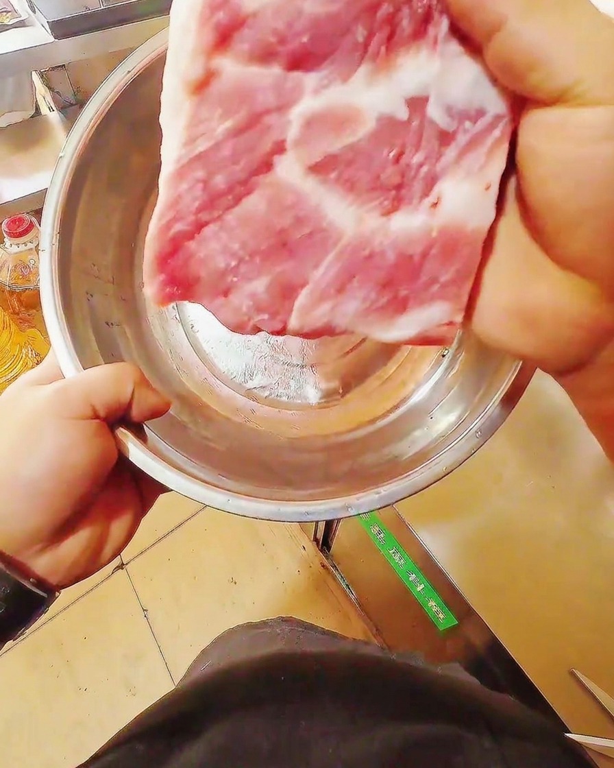 Un couteau aiguisé découpant un beau morceau de poitrine de porc crue sur une planche en bois.