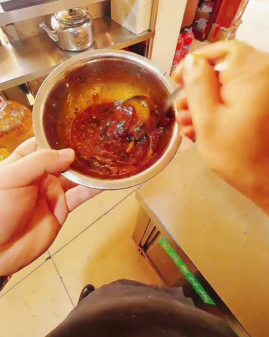 Gros plan dun bol en inox contenant une marinade rouge sombre, mélangée avec une cuillère.