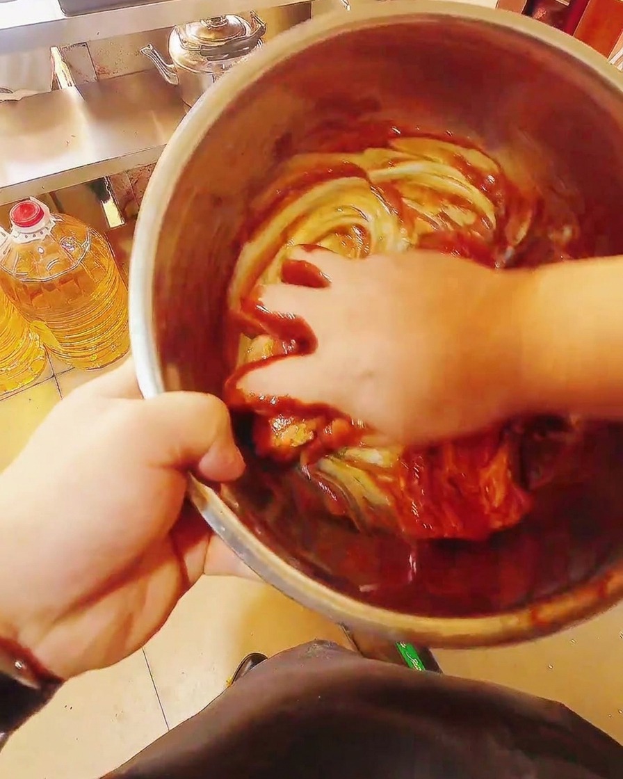 Lanières de porc crues mélangées à la main dans un grand bol avec une épaisse marinade rouge brillante.