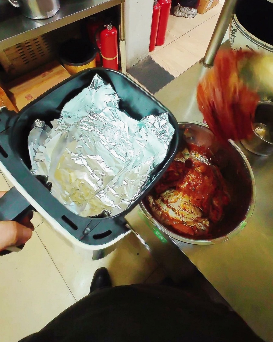 Lanières de porc marinées disposées à plat sur une feuille daluminium dans le panier dun Air Fryer.