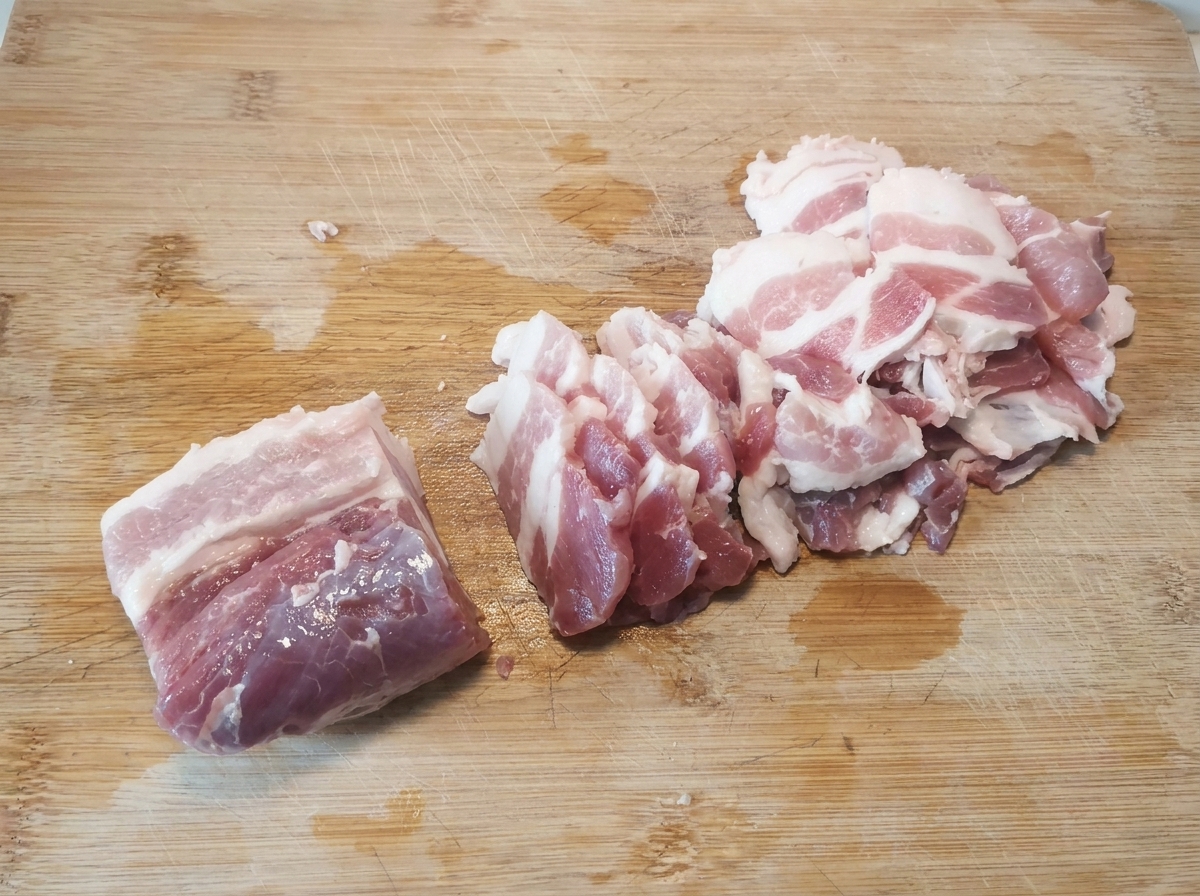 Fines tranches de poitrine de porc crue soigneusement disposées sur une planche à découper en bois après avoir été coupées.